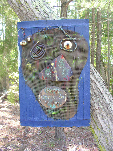 Found-metal face with spiral eyes framed in blue wood