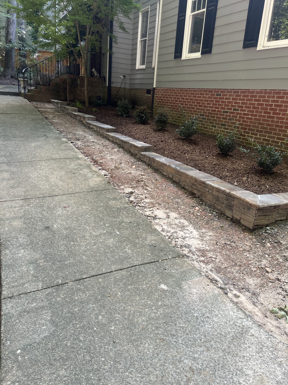 Low stone planting wall beside a residential walk and freshly mulched bed